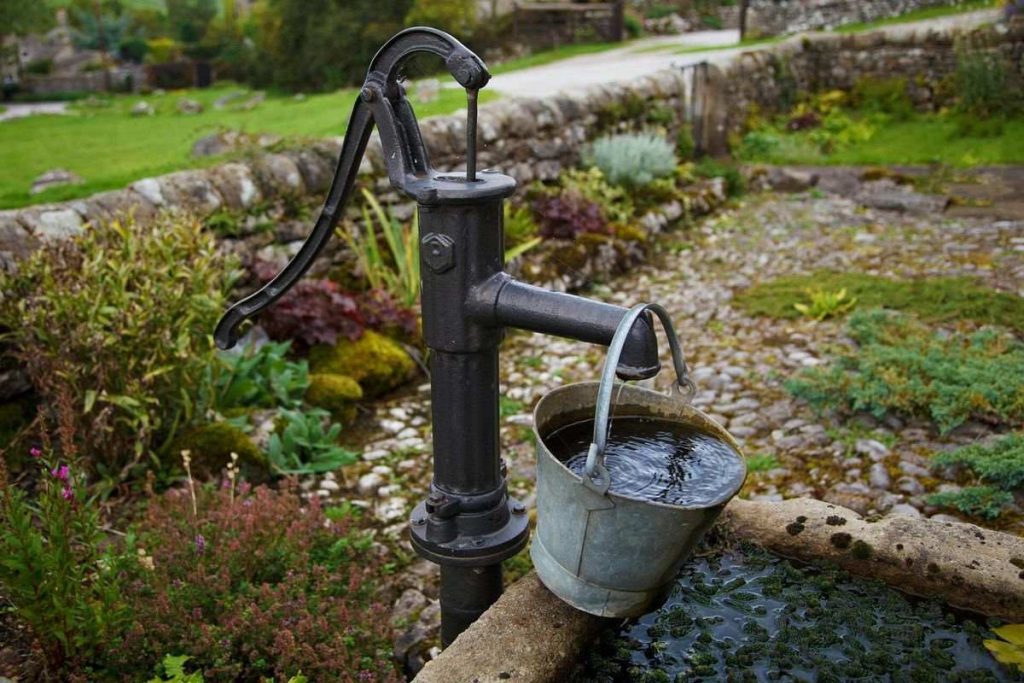 old fashioned water pump with a metal bucket of water hanging from the spout