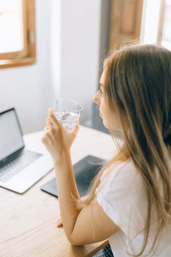 woman sitting in front of computer holding water glass