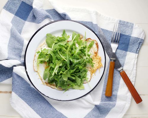 a plate of fried eggs with a large helping of arugula leaves on top