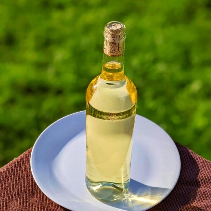 A bottle of golden yellow dandelion wine in the sunlight.
